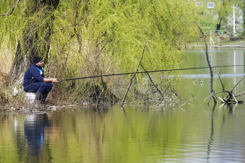 Rybaření na jaře, rybář sedící u jezera držící prut